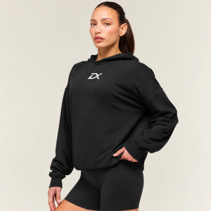 Female model wearing a black Drimex Sports Conditioning Club oversized hoodie with matching shorts and sneakers